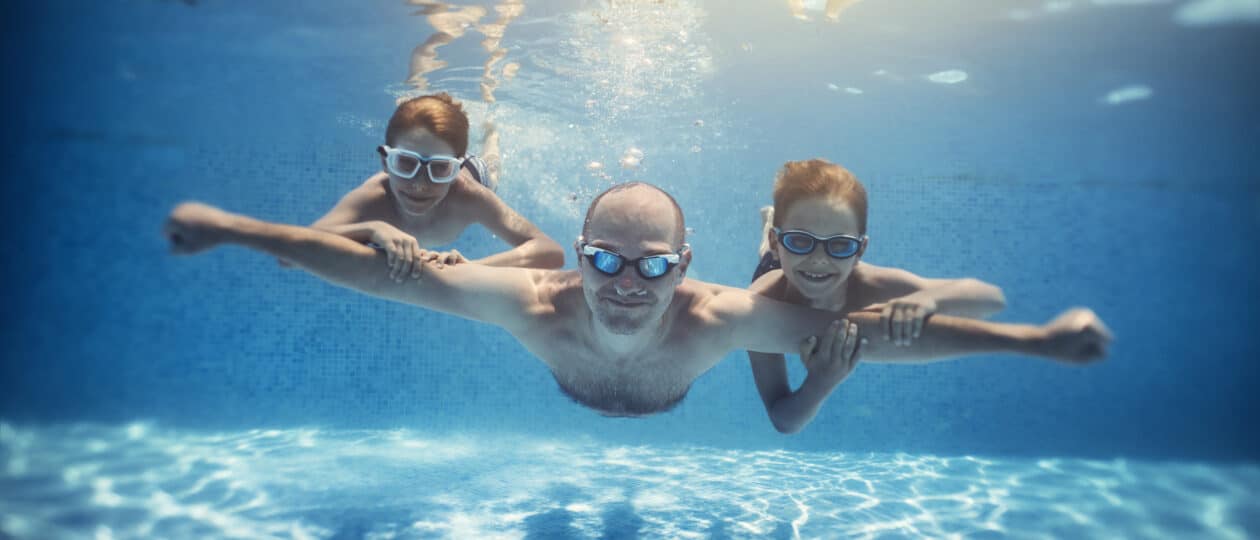 Father and sons playing underwater in resort pool. Family is playing underwater superheroes.
