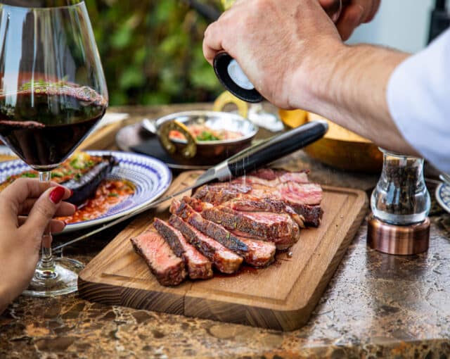 Seasoning juicy medium rare steak steak with salt grinder, cut on wooden board on restaurant table
