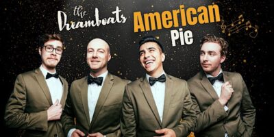 Four men in matching olive green suits and black bow ties, posing with smiles against a sparkling golden backdrop with the text "The Dreamboats American Pie" overlaid in a decorative font, along with a musical note motif.