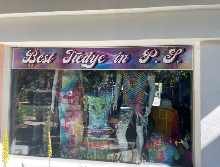 A storefront window with a sign reading "Best Tie-dye in P.S." displaying various tie-dyed clothing items on mannequins.